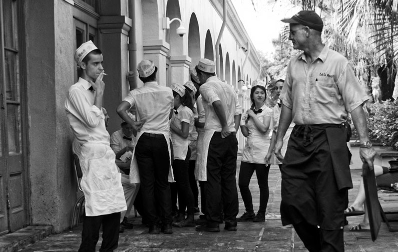 Black and white photo of a unch of workers in hats and aprons taking a smoke break