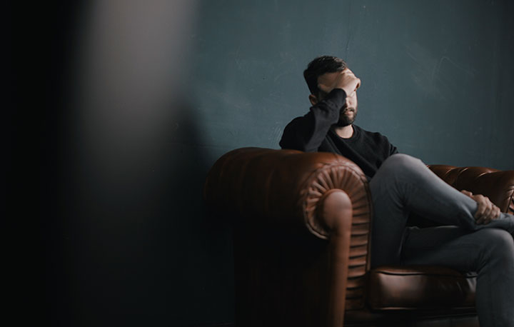 a man holds his head while sitting on a couch