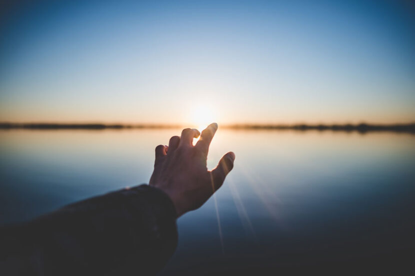 Hand reach toward sunlight over water