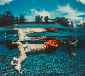 White man underwater wearing red shorts with face above the surface