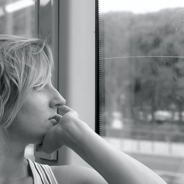 Black and white photo of person looking out a window with their chin resting in their hand