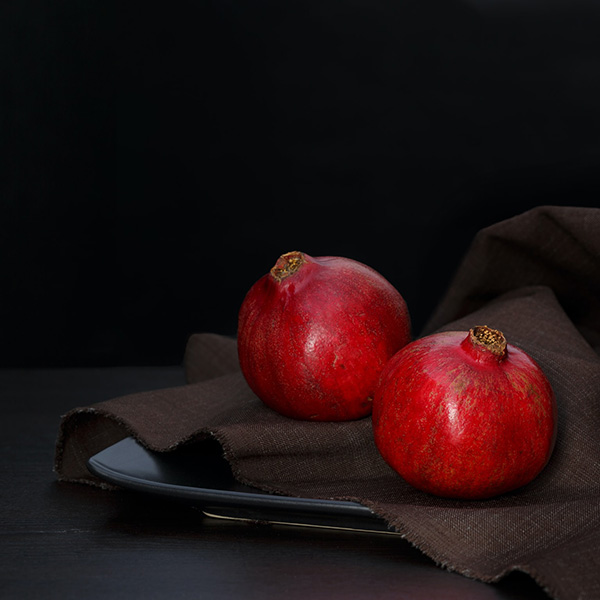 Two pomegranates on dark cloth with a black background