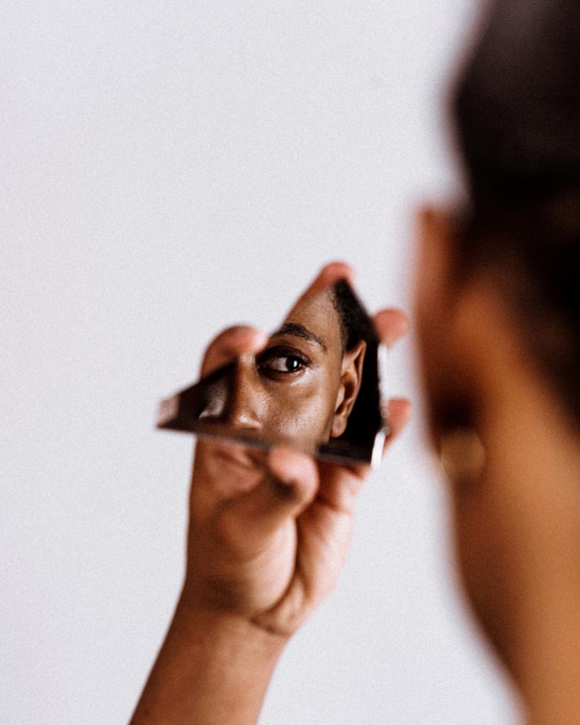 A Woman with Dark Skin Staring at her Face in a Broken Piece of Mirror