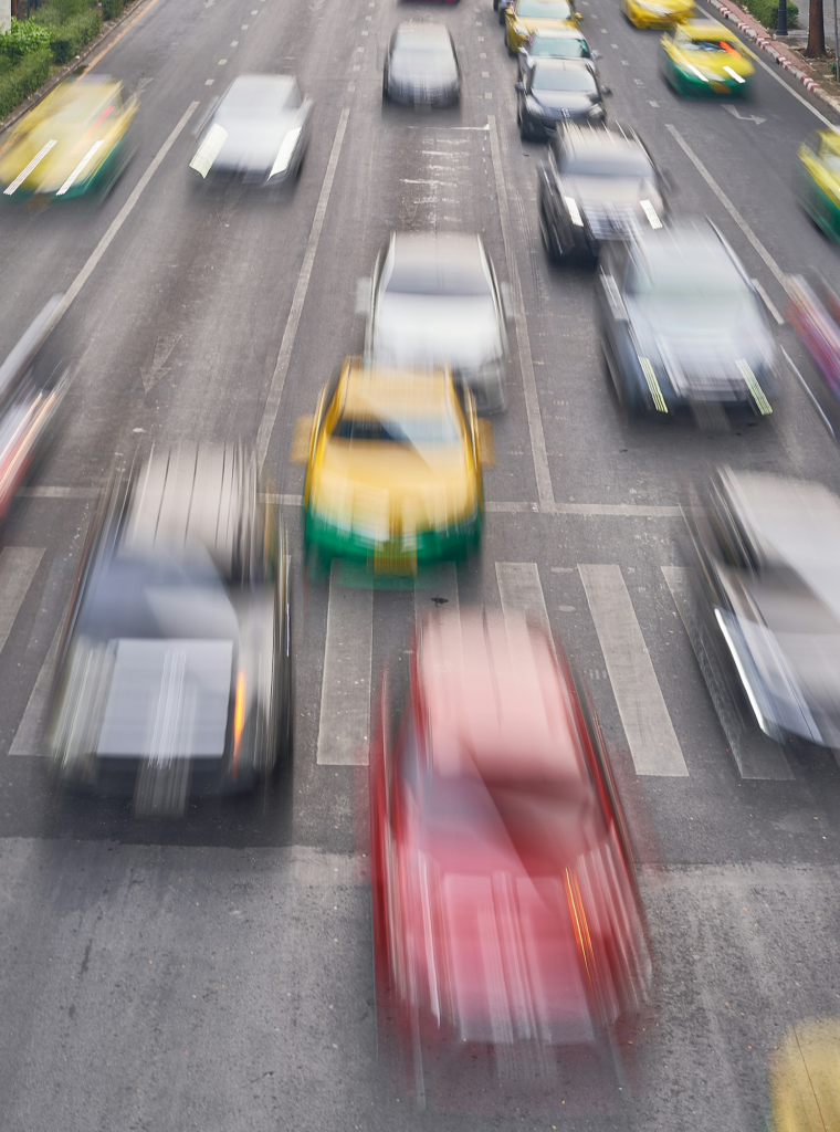 Five lanes of heavy traffic on a highway, the cars blurred to give the impression they are moving fast.