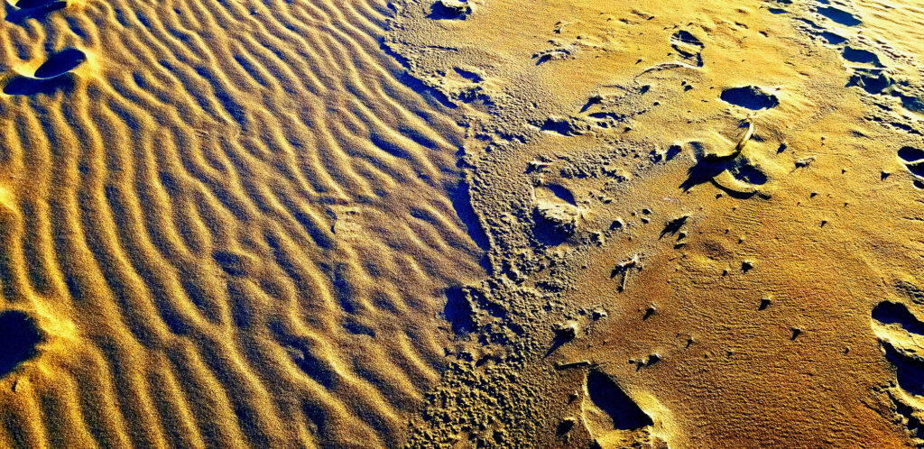 Ridges left by waves and shadowy footprints on a beach strand