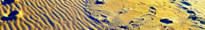 Ridges left by waves and shadowy footprints on a beach strand