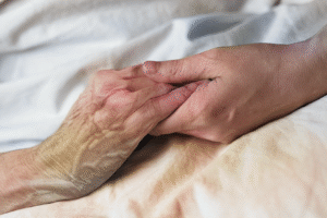 Elderly hand holding younger hand across bed linens.