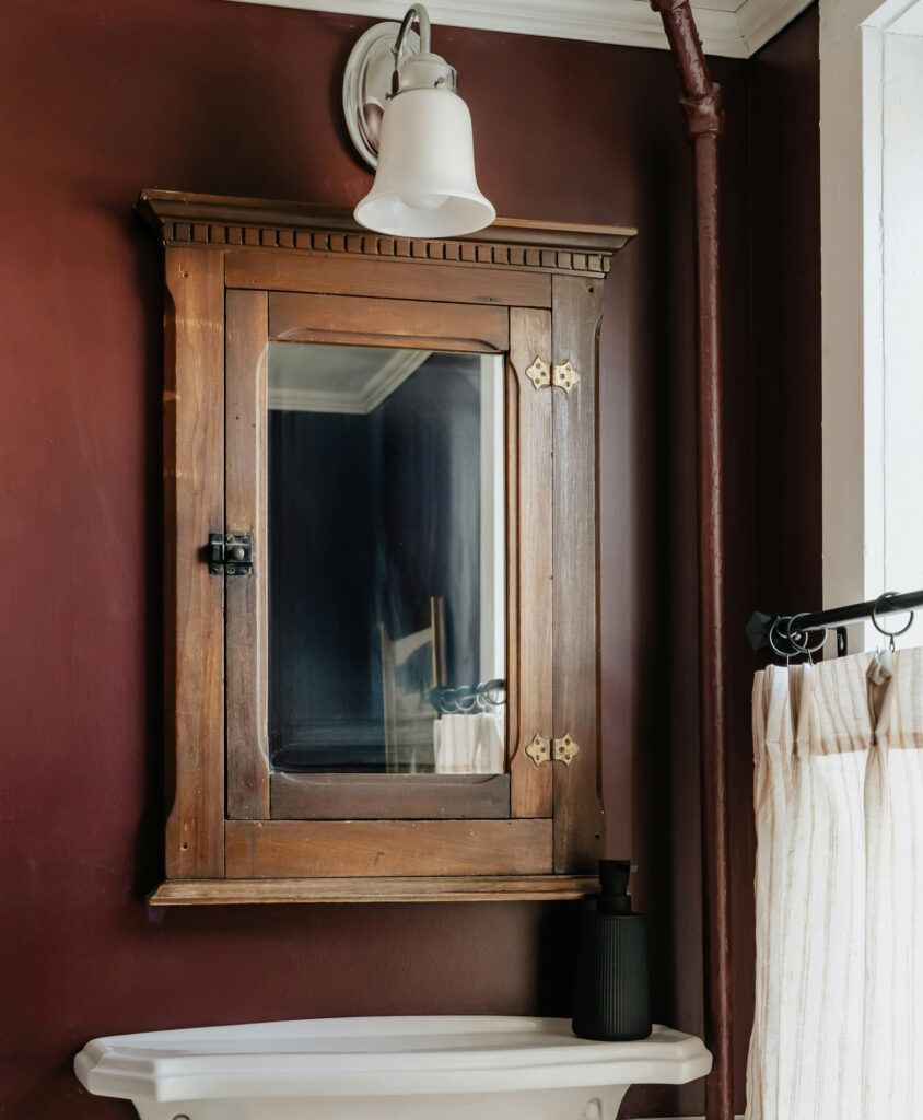 A photo of a mirrored, wood-framed bathroom cabinet hung over a sink.