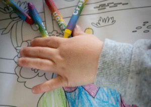 Young hand selecting from color crayons on coloring sheet.