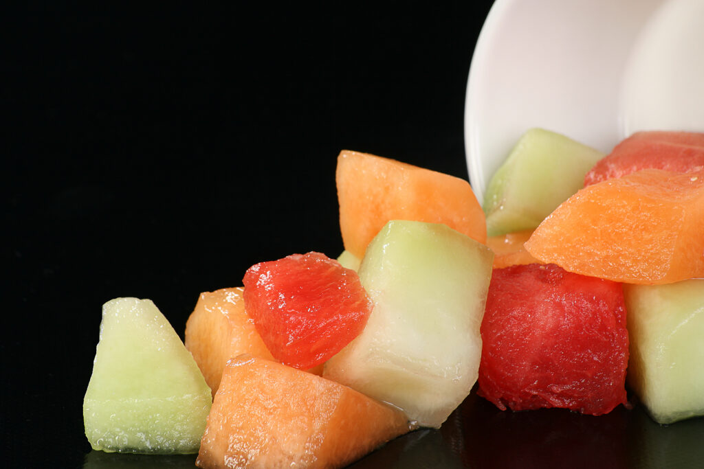 Photo of cantaloupe, honeydew melon, and watermelon chunks tipping out of a bowl and spreading onto a counter