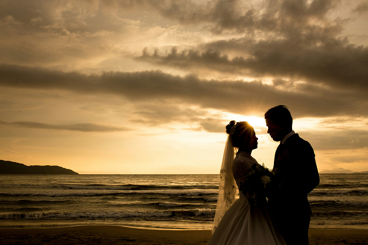 Photo of a bride and groom on a tropical beach silhouetted by the sunset