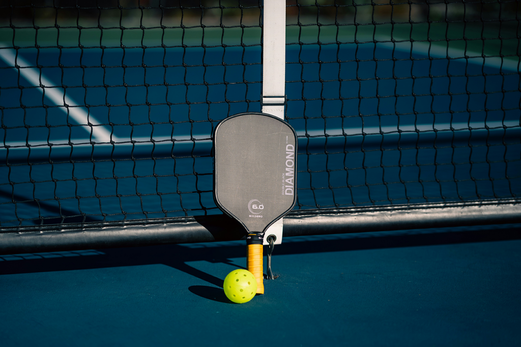 Photo of a pickle ball and paddle leaning against the net on the court