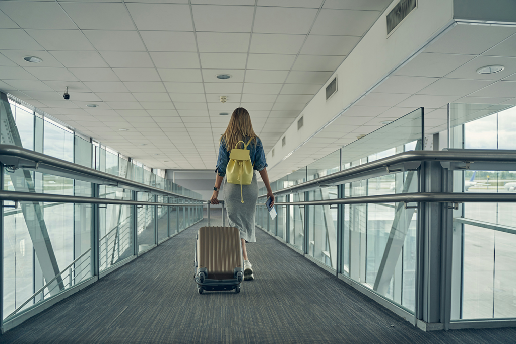 Photo of a young woman walking away through an airport towing her wheeled luggage.