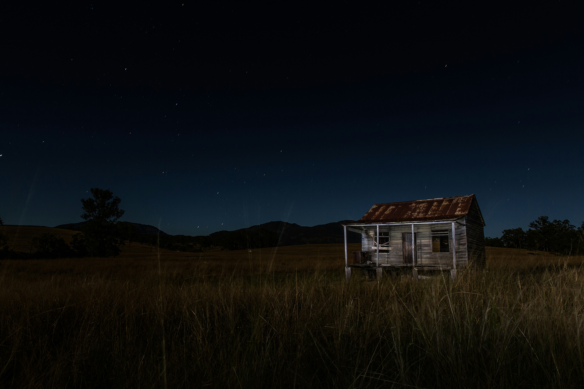 Rundown shack in a field on edge of foothills at dusk.