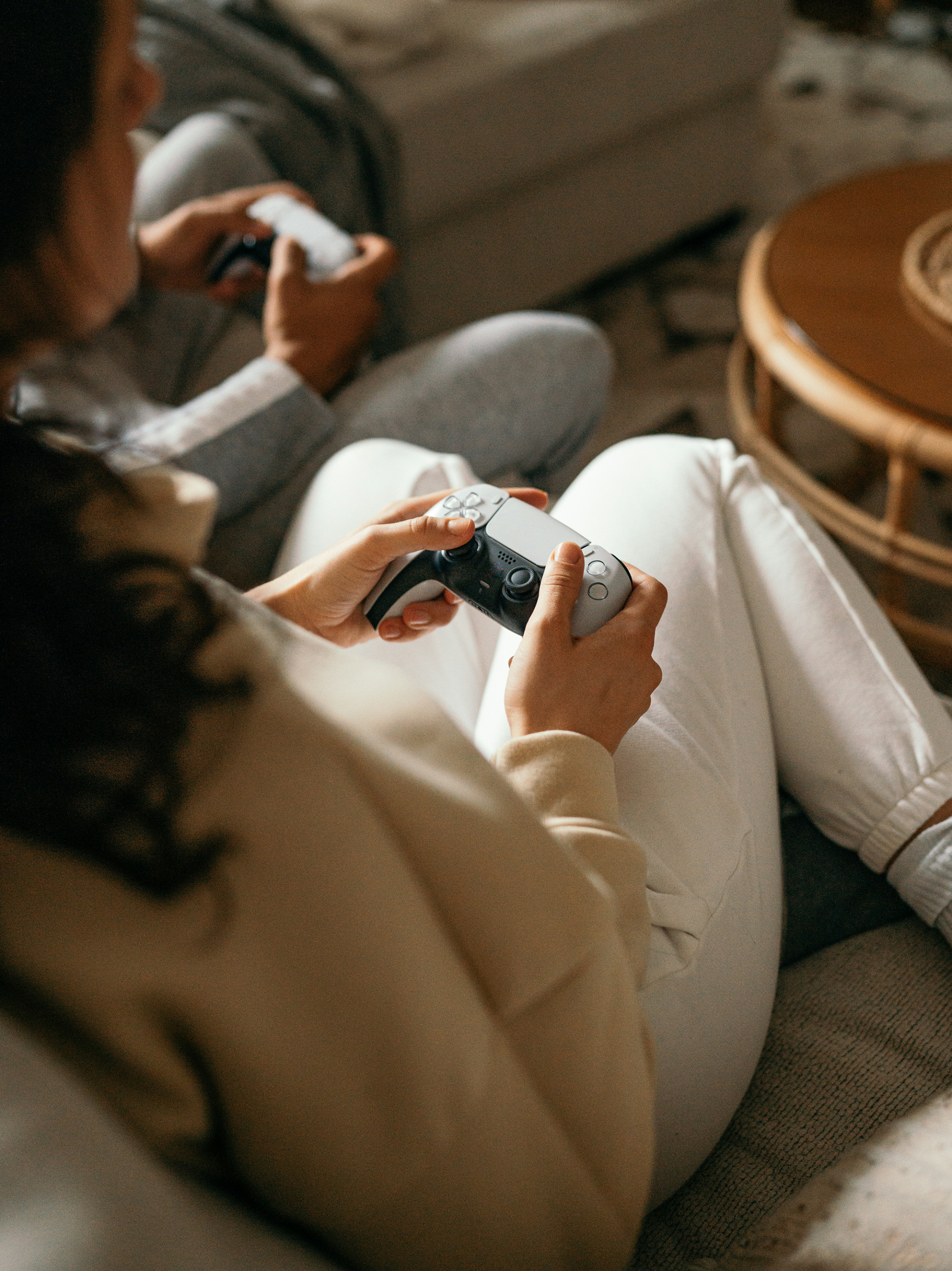 Photo of a woman and a teenager sitting on a sofa with video game controllers playing a game.