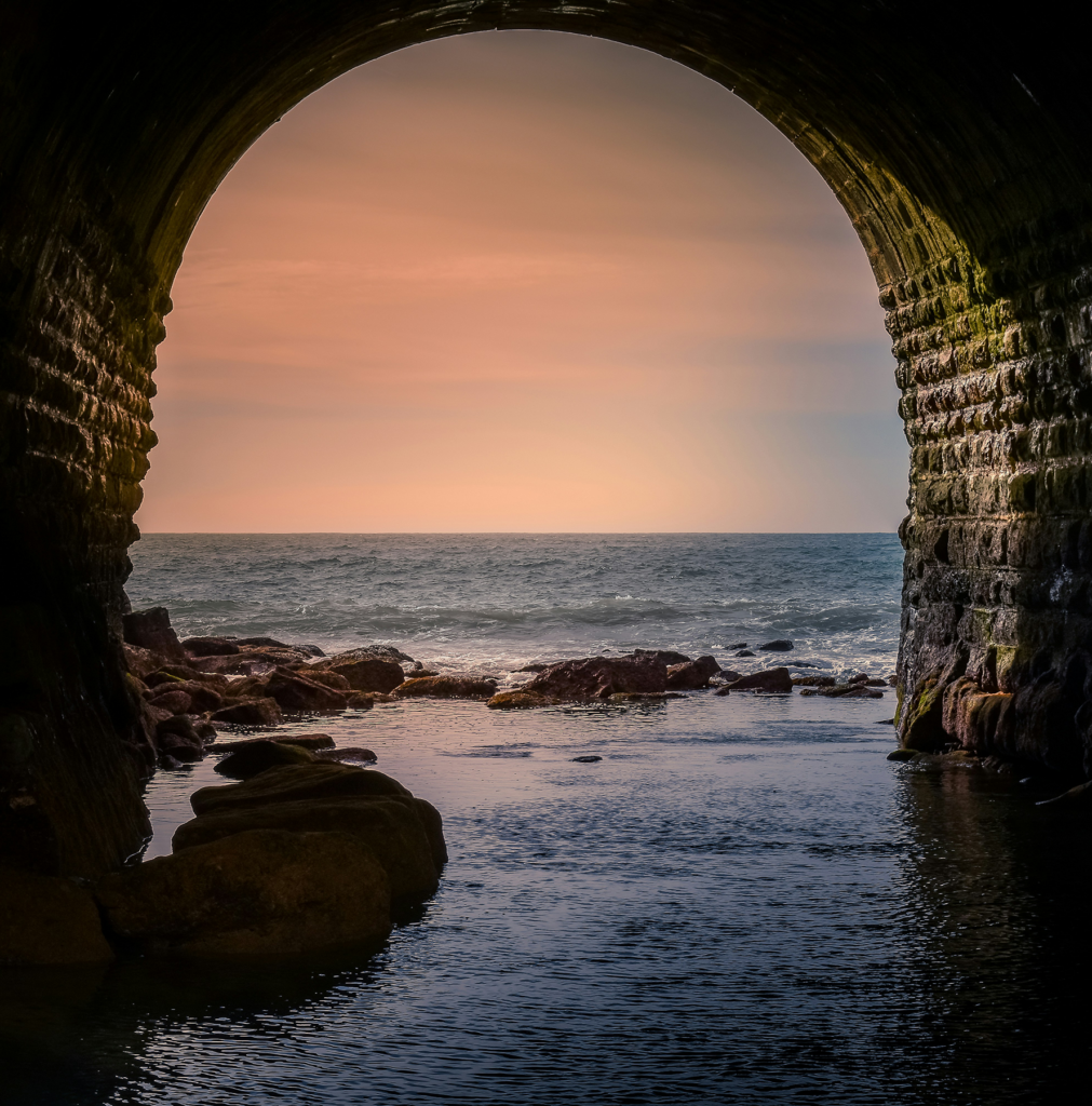 Sunset view through brick tunnel out to rocky ocean shoreline